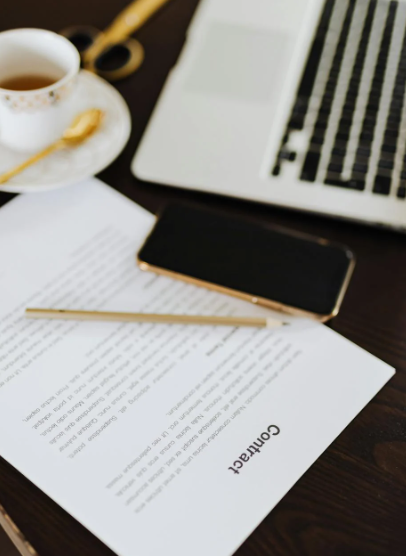 This image shows a contract, a mobile phone, a laptop, and a cup of tea.