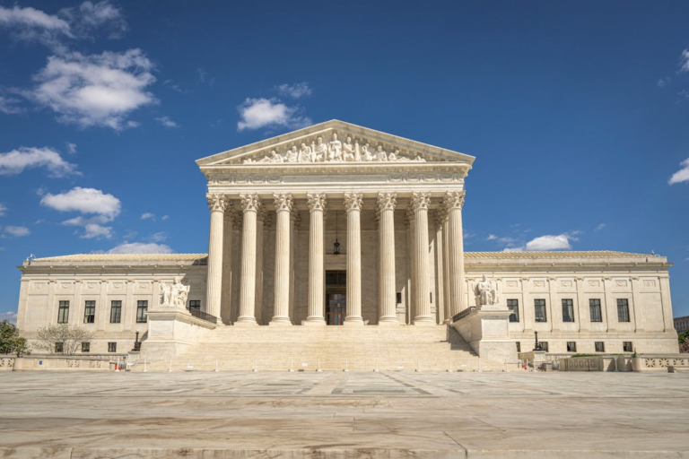 Stone courthouse exterior with tall columns and a clear blue sky visible in the background