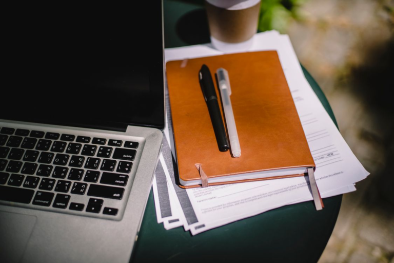 An image of a laptop and a notebook next to it with pens on top