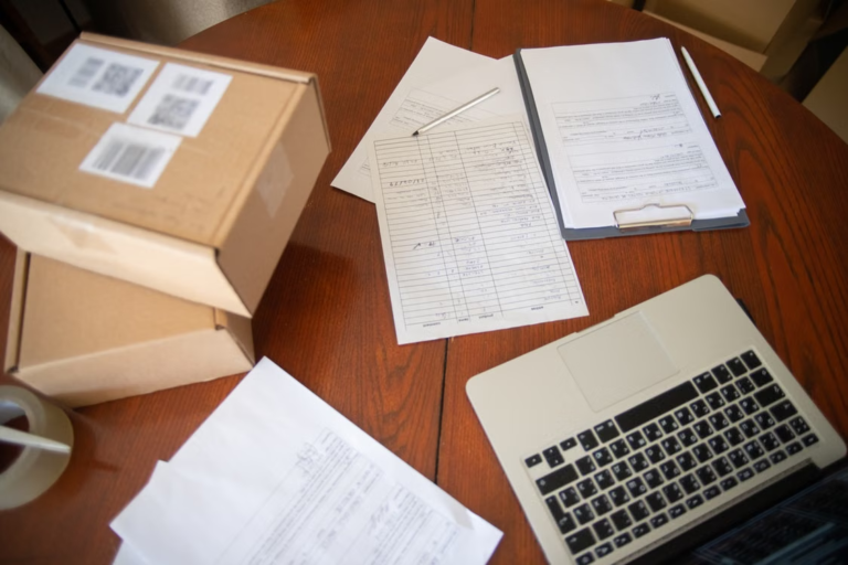 An image of papers, boxes, and a laptop on a brown wooden table