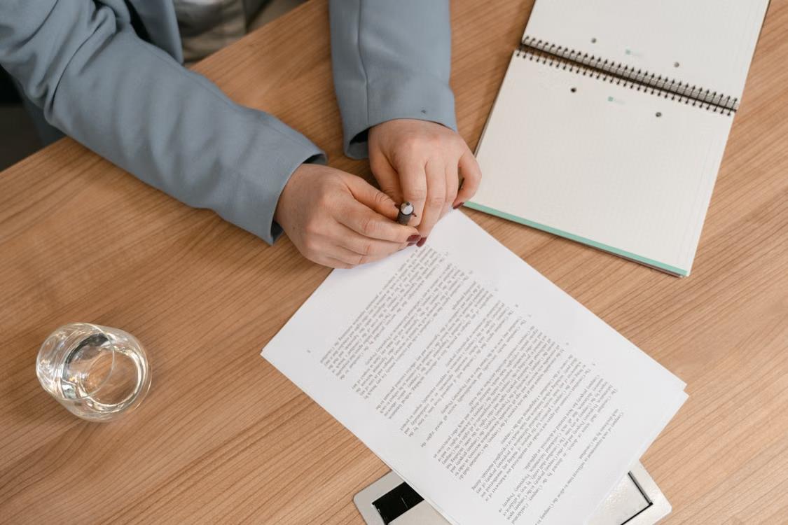 An image of a person holding a pen and sitting at a desk with papers on it