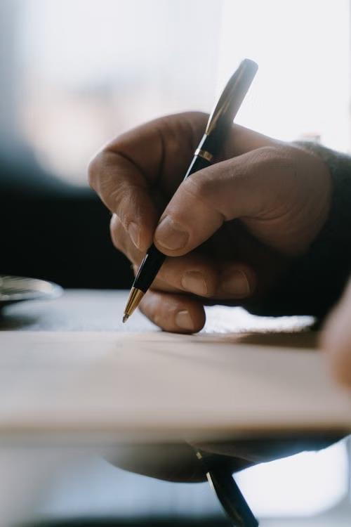 An image of a person pointing at something with a pen on paper