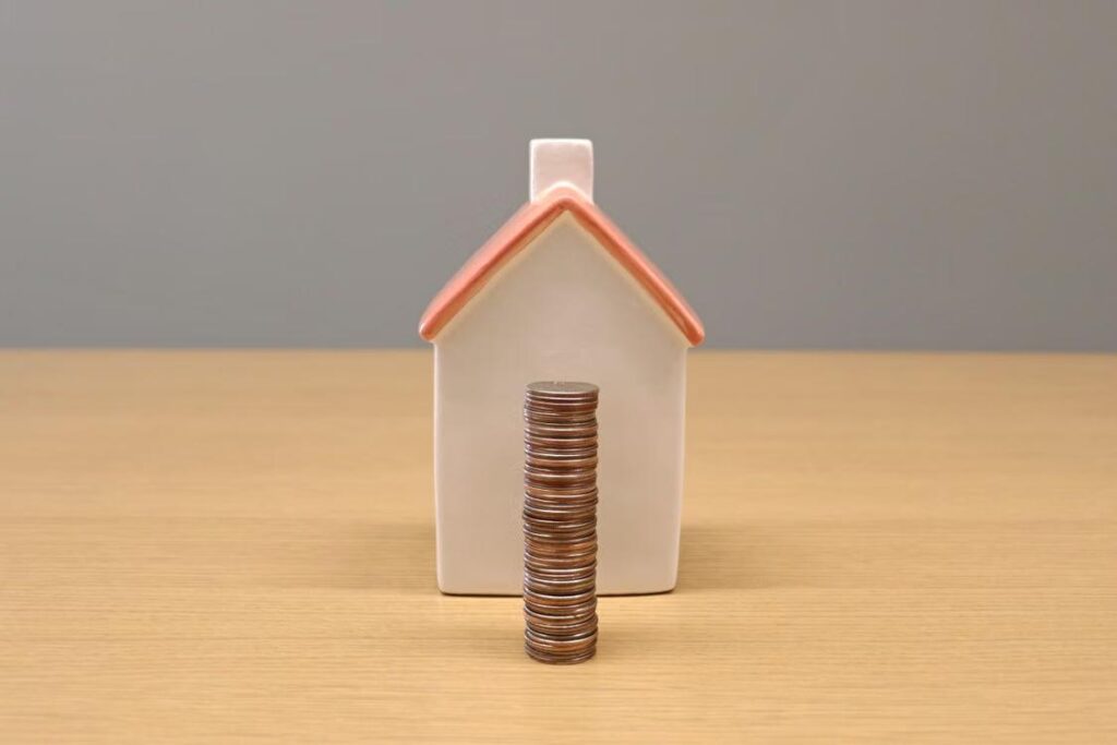 An image of a wooden house behind a stack of coins