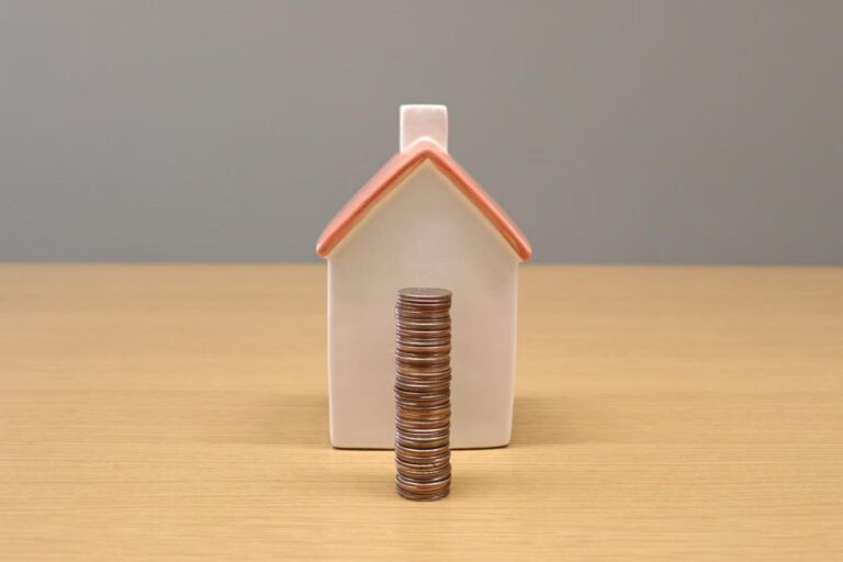 An image of a wooden house behind a stack of coins