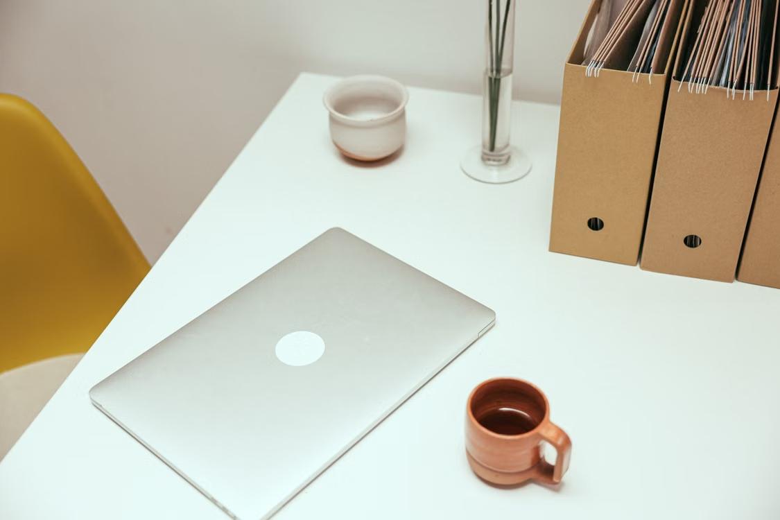 Closed laptop beside a coffee cup on a wooden table