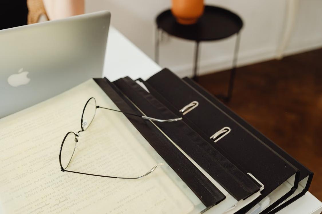 Eyeglasses resting on black binders beside a laptop