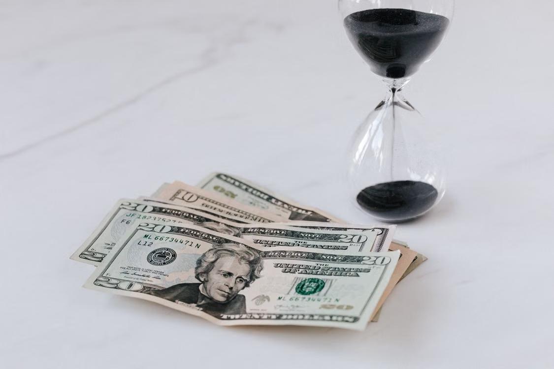 Sandglass beside a pile of dollar bills