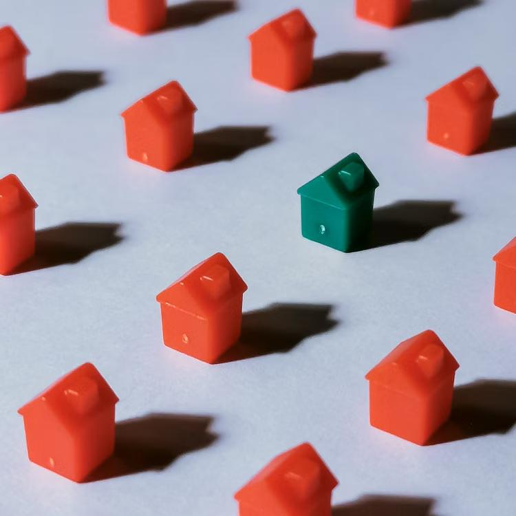 Small red houses arranged on a pale surface with one green house