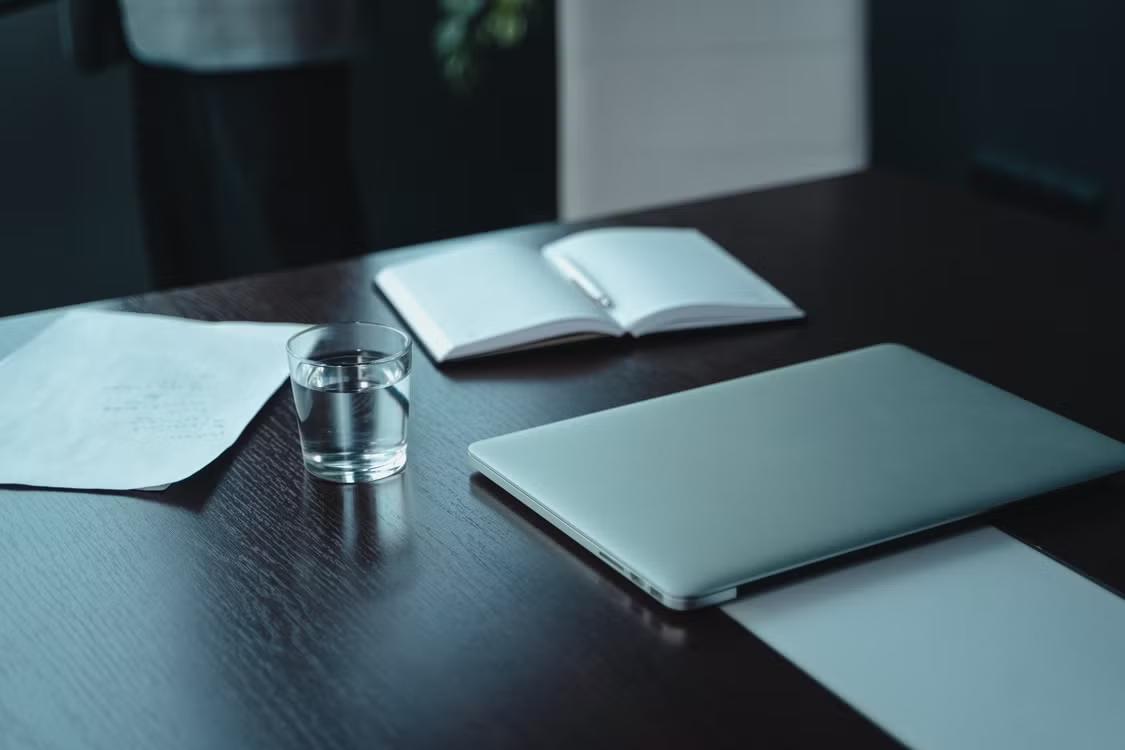 Closed laptop, notebook, and glass of water on a dark table