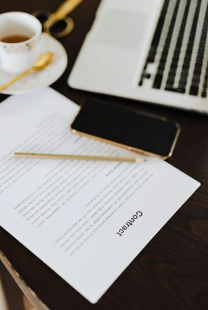 Contract on a table beside a laptop, phone, and coffee cup