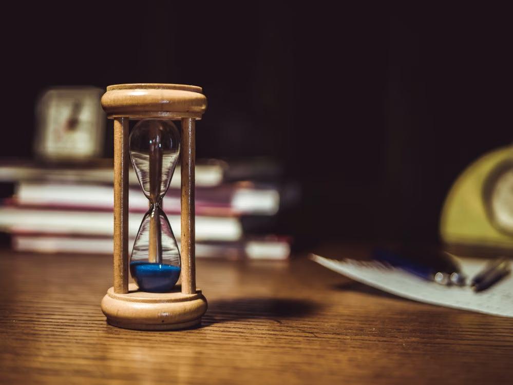 Wooden hourglass on a table beside books