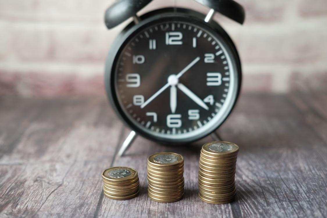 Alarm clock beside stacks of coins on a wooden table