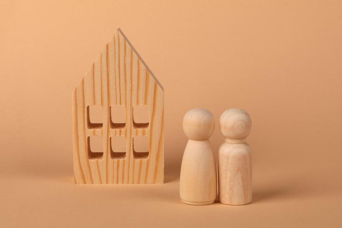 Wooden house and two wooden figures on a peach background